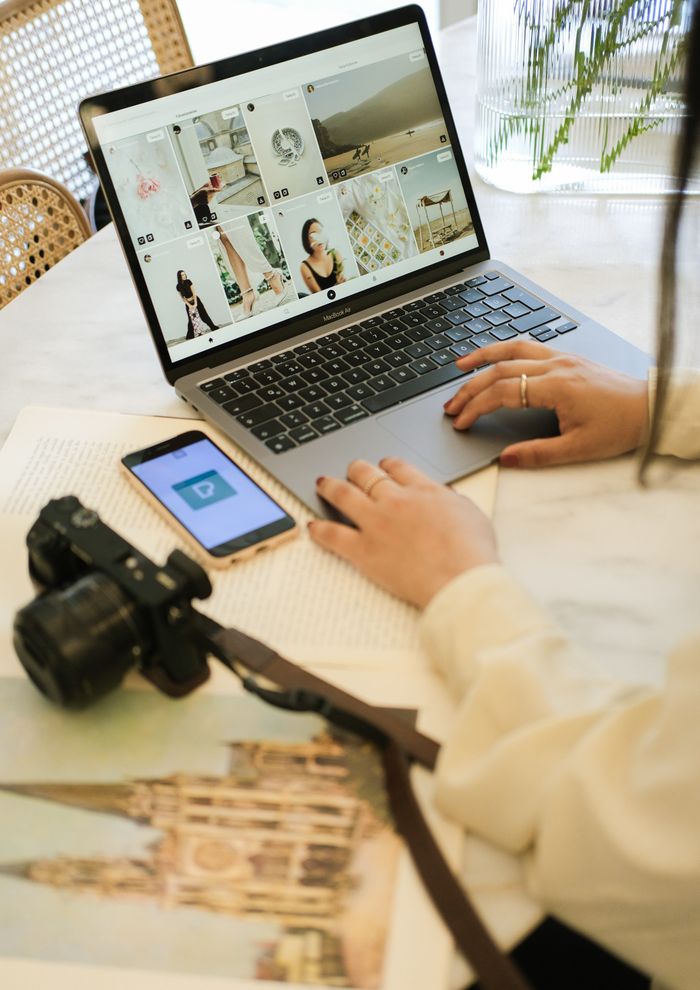 gallery-3 Una mujer trabaja con una laptop, con una cámara y un smartphone sobre el escritorio, en un ambiente interior acogedor.