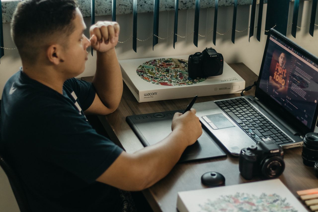Un fotógrafo trabaja en un entorno creativo con una laptop y una tableta Wacom, concentrado en la edición de fotos en interiores.